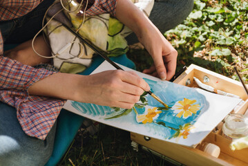Closeup of woman's hands paiting in oils bright flowers outdoors