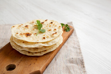 Homemade Roti Chapati Flatbread on a rustic wooden board on a white wooden surface, side view. Copy space.