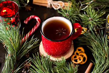 New year's tea party with spices. Red mug with tea surrounded by garlands, fir branches and spices	
