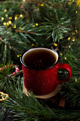 New year's tea party with spices. Red mug with tea surrounded by garlands, fir branches and spices	
