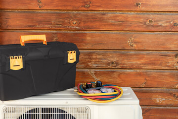 Images of an air conditioner and tools for its repair and maintenance on the background of a wooden wall.