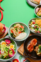 Variety of food dishes on bright green background. Table covere with food flat lay, top view, frame.