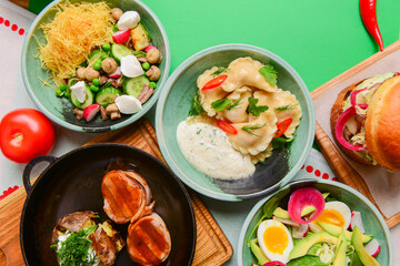Variety of food dishes on bright green background. Table covere with food flat lay, top view, frame.
