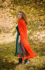 Naklejka premium Woman in green velvet romantic dress and red hood, Halloween style for girls, autumn nature at background