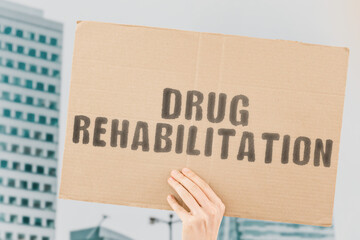 The phrase " Drug rehabilitation " on a banner in men's hand with blurred background. Addiction. Rehab. Problem. Drugs. Recovery. Help. Support