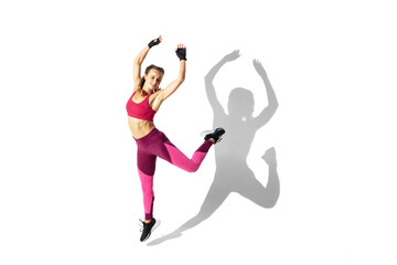 Jumping. Beautiful young female athlete practicing on white studio background, portrait with shadows. Sportive fit model in motion and action. Body building, healthy lifestyle, style concept.