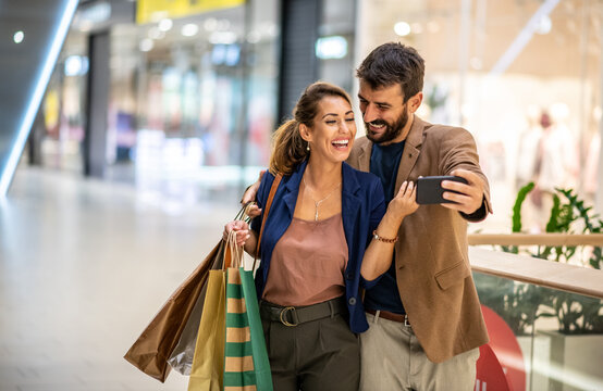 Young handsome fashionable couple standing in shopping mall and taking selfie.