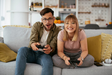 Boyfriend and girlfriend playing video game with joysticks in living room. Loving couple are playing video games at home...