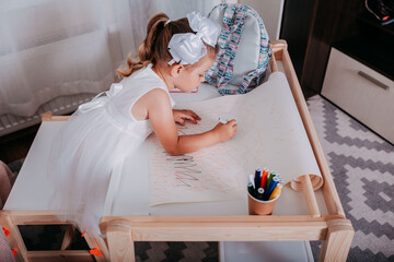 Little girl in the school near the school desk. A girl writes on the paper. School supplies on the desk.