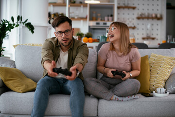 Obraz premium Boyfriend and girlfriend playing video game with joysticks in living room. Loving couple are playing video games at home...