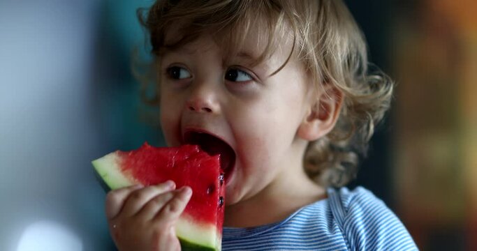 Toddler eating watermelon fruit. Close-up child taking a bite of juicy watermelon