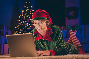 Shocked crazy elf read x-mas congratulation on laptop floor wear green costume in christmas evening...