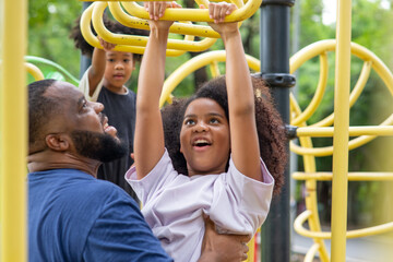 Happy affectionate mixed race family. African man father carrying little daughter playing at playground in the park. Dad and two child girl enjoy and having fun together in outdoor weekend vacation.