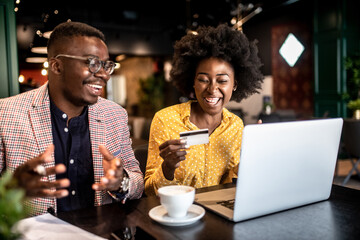 Attractive smiling african couple sitting in cafe and purchasing over internet things for house.