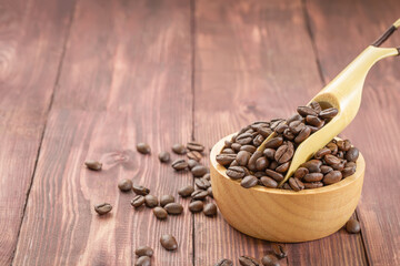 Coffee beans roasted in a bean scoop on a wooden bowl full of coffee beans over wooden background.