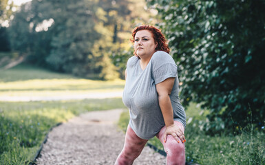 Chubby sportswoman stretching leg and preparing to running outdoors.