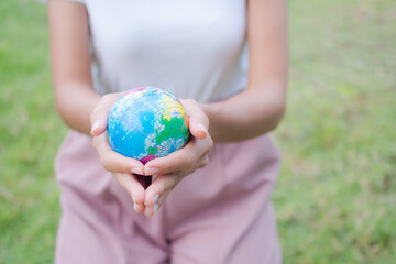 Close up hand woman holding earth on blur image of grass background. Environmental conservation Earth Day concept. copy space.
