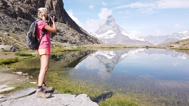 Alpine meadows around Matterhorn reflected on Riffelsee Lake. Backpacker tourist woman photographer taking pictures at Matterhorn mountain. Tourism in Zermatt, Canton of Valais, Switzerland.