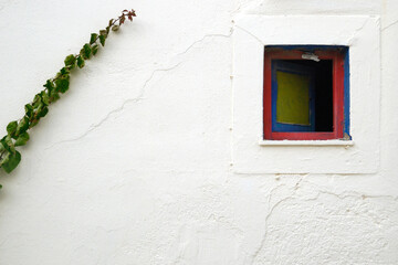 Biała ściana greckiego domu z małym kwadratowym oknem i pnącą rośliną - obrazy, fototapety, plakaty