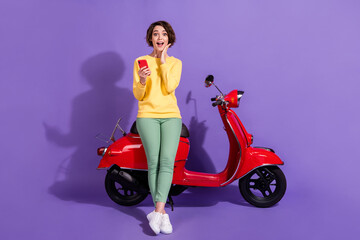 Fototapeta na wymiar Full length body size view attractive amazed stunned cheerful glad girl sitting on bike using device browsing post app 5g isolated over bright vivid shine vibrant lilac violet purple color background