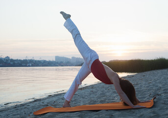 Young woman doing yoga exercises on the beach in the morning. Rest from the city noise