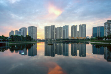 Obraz premium Buildings with reflections on lake at sunset at Thanh Xuan park. Hanoi cityscape at twilight period