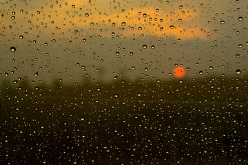 Krople deszczu na szybie na tle zachodzącego słońca.