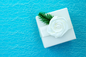 White gift box on a blue background. Christmas and New Year background. A gift decorated with a white ribbon and a branch of a Christmas tree. Place for your text. View from above.