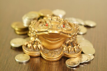 Fototapeta na wymiar A metal toad next to a stack of coins. Symbol of happiness and financial success.