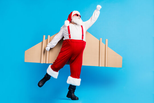 Full length photo of stylish modern white grey hair bearded santa claus fly craft wings 0on x-mas christmas time noel night wear red costume isolated blue color background