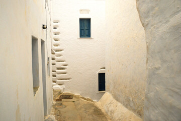 Wąska uliczka na greckiej wyspie Amorgos. Białe ściany, niebieskie okna.