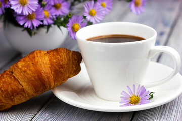 French croissant with a cup of coffee on a white wooden table.