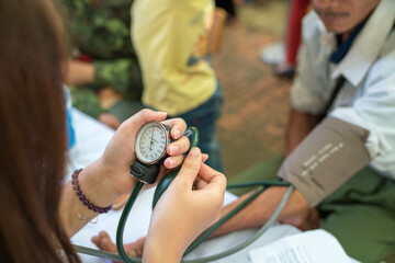 Volunteer nurse measuring blood pressure of poor Asian people outdoors closeup