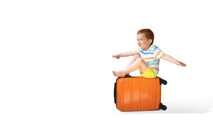 One red-haired boy of 3 years in bright clothing sits on an orange suitcase hand side depicts the plane isolated