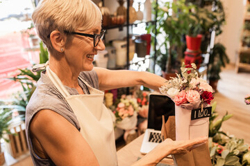 Senior female florist working in her flower shop and prepares online orders using laptop.
