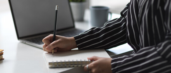 Female hand writing on blank notebook while working on white office desk