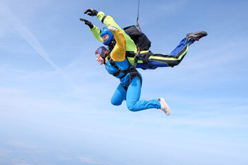 Fototapeta na wymiar Skydiving. Tandem jump. Happy girl and her instructor are falling in the blue sky.