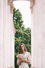 A beautiful Ukrainian bride, in a cute dress and holding a bouquet of flowers. Her face is half covered with hair and she looks at the flowers.
