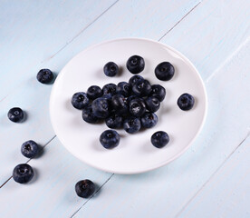 blueberries on a white plate on a blue wooden table background. concept of fresh and healthy food, harvesting.
