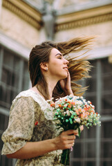 Vertical portrait of a European girl who is spinning with happiness holding a festive bouquet in her hands. Against the background of an old building
