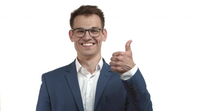 Attractive happy businessman in blue suit and glasses, looking excited and showing thumbs-up, smiling as approve something very good, like and recommend product, standing over white background