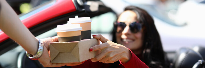 Woman in car picks up coffee from courier. Fast beverage delivery concept