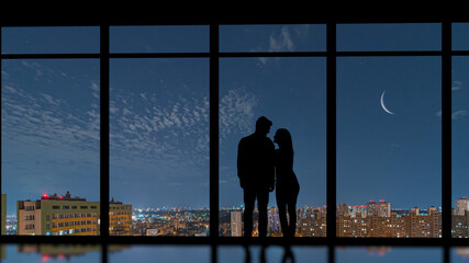 Fototapeta na wymiar The couple standing near the panoramic window on a city moon background