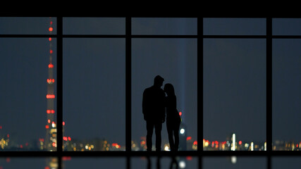 Fototapeta na wymiar The couple standing near the panoramic window on the city background