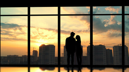 The couple standing near the panoramic window against the beautiful sunset