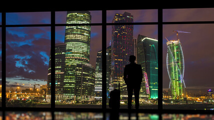 The man with suitcase standing near a panoramic window on skyscrapers background