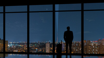 Fototapeta na wymiar The man with a suitcase standing near a panoramic window against an evening city