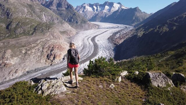 Tourist woman from viewing platform looking Alpine glacier. Aletsch Glacier from Moosfluh viewpoint in summer, Valais Canton, Switzerland, Europe. Outdoor activities. Trekking in the Swiss Alps.