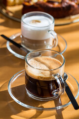 Two cups of coffee and cappuccino with cake on wooden table