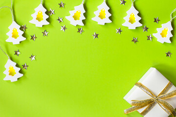 White garland in the form of Christmas trees, confetti in the form of stars and a gift box, with a shiny silver-gold ribbon on a green background. Christmas, New year. Flat lay, copy space